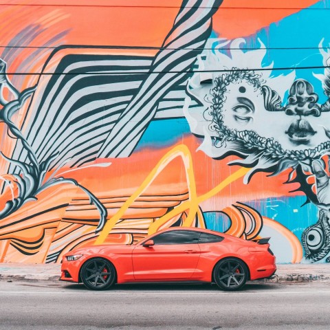 red car parked beside wall with graffiti J