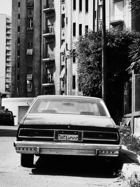 a black and white photo of a car parked on the side of the road 0MOrrnDwp