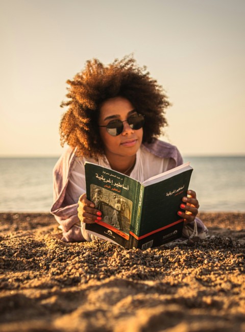 a person with curly hair holding a book on a beach