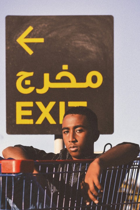 a man sitting in a shopping cart in front of a exit sign
