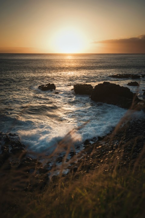 the sun is setting over the ocean and rocks