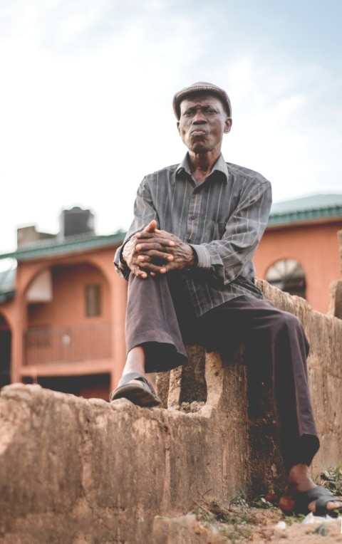 man in gray button up shirt and black pants sitting on brown rock during daytime